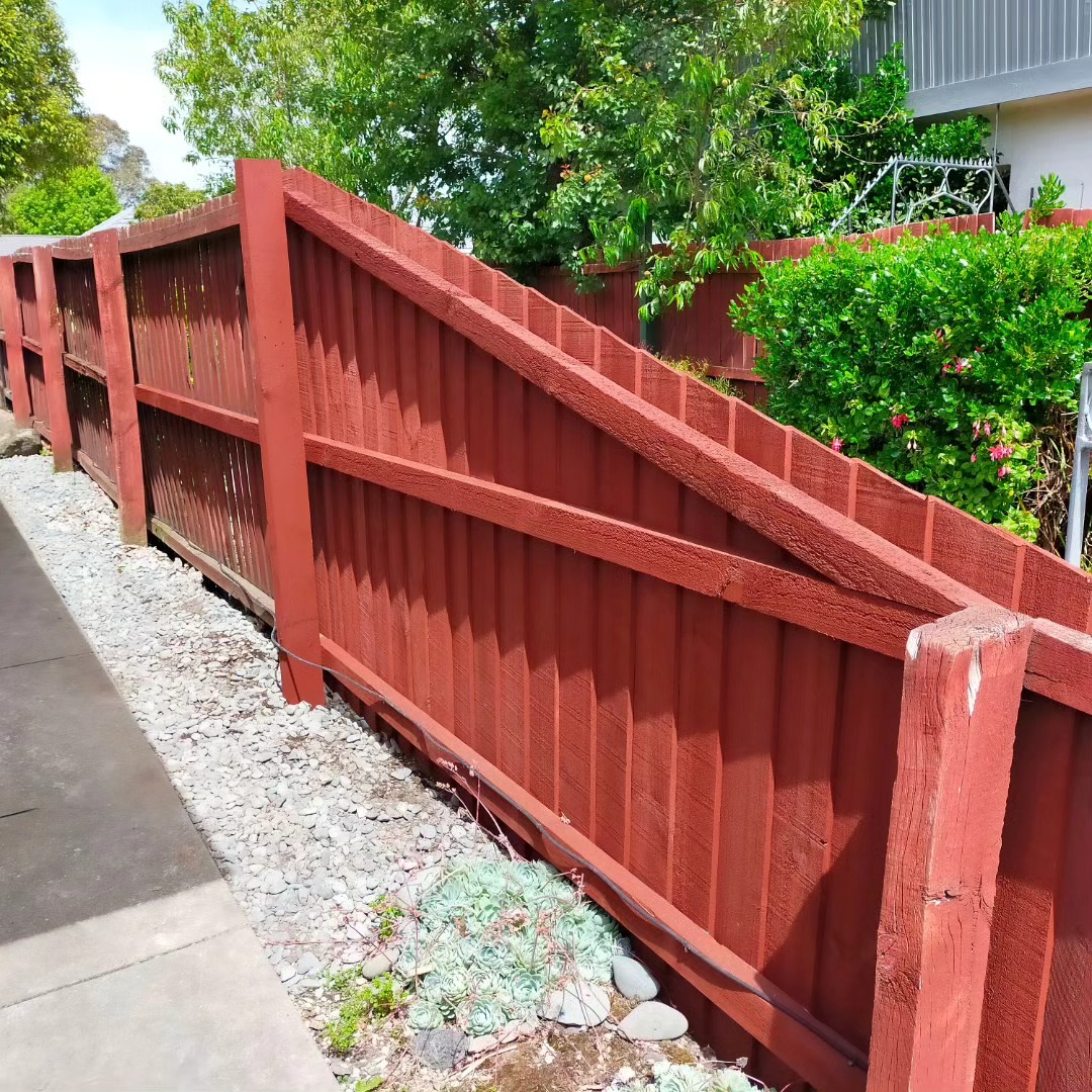 Repaired red paling fence along a gravel path